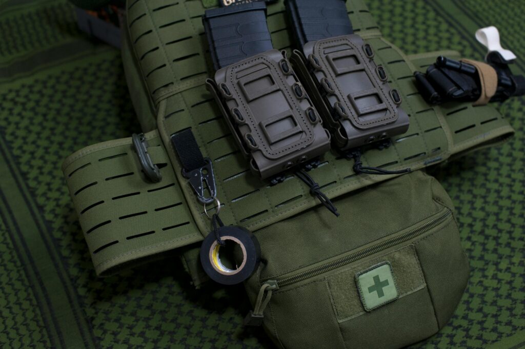 Close-up of a green tactical military vest with two pouches and medical equipment.